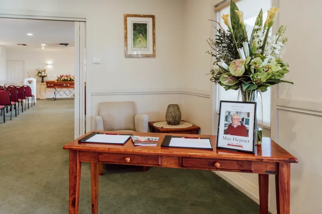 Timber welcome table in the foyer featuring a large floral arrangement, condolence registers, and a framed tribute photo at 199 Ormond Rd, East Geelong.