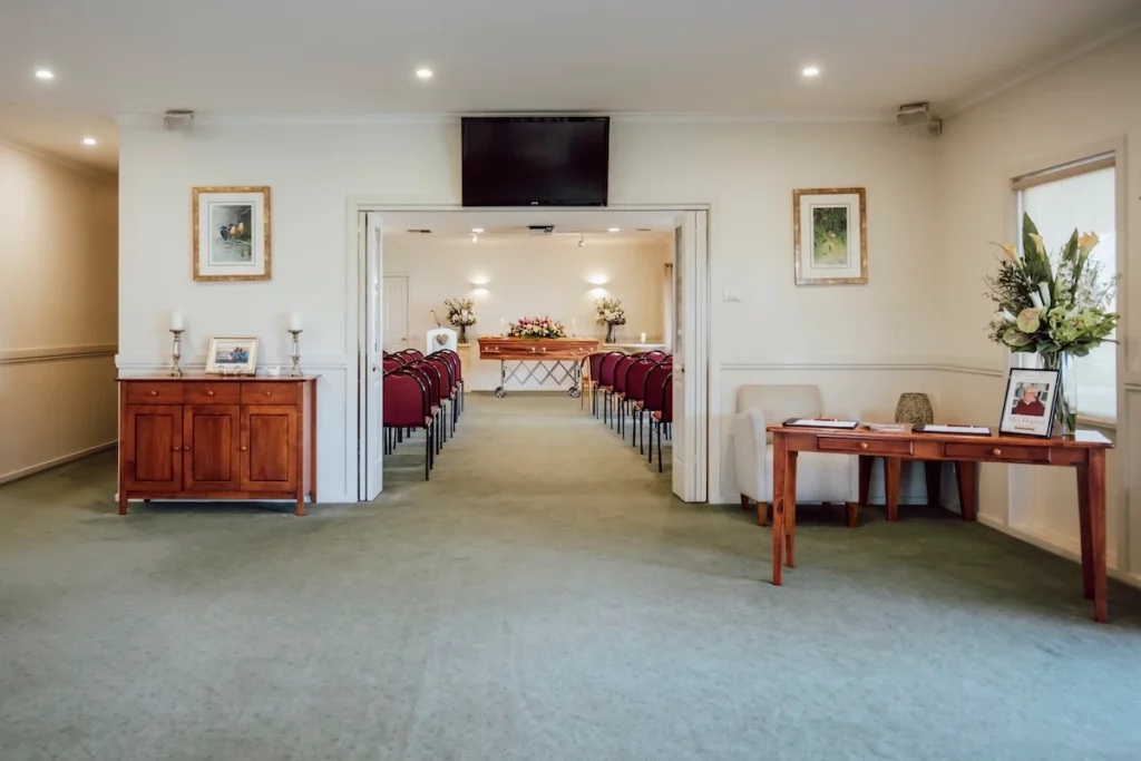 Foyer entrance with an overhead AV tribute screen and double doors opening into the East Geelong Small Chapel seating area at Jonathan Hepner Funerals.