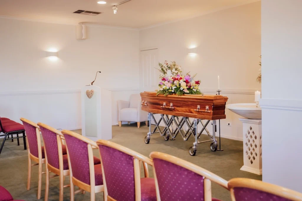 Front view of the speaker lectern, candle stands, and polished wooden casket with a bright floral bouquet inside the East Geelong Small Chapel at 199 Ormond Rd.
