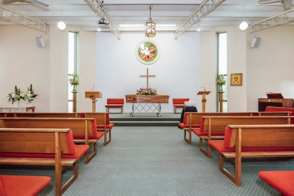 Symmetrical view down the centre aisle showing timber pews with red cushions leading to the main sanctuary stage at Jonathan Hepner Funerals' East Geelong Uniting Chapel, located at 199 Ormond Rd, East Geelong.
