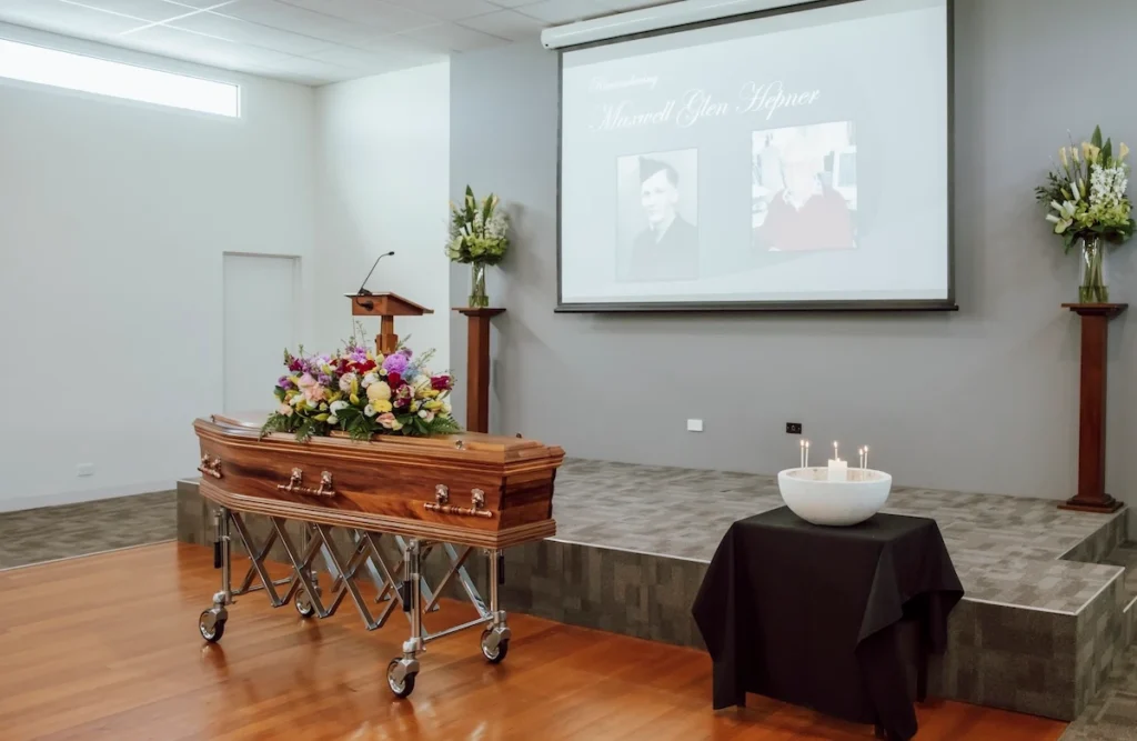 Angled perspective of the raised presentation stage, timber casket, and memorial candle display inside the East Geelong Uniting Hall at Jonathan Hepner Funerals' 199 Ormond Rd location.