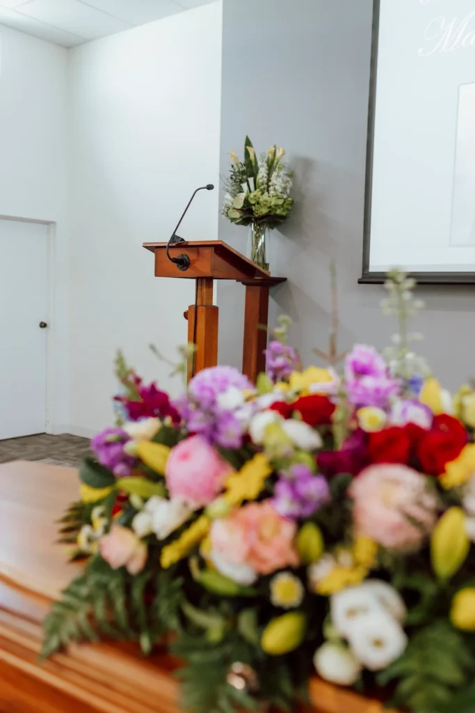 Close-up view of a vibrant casket floral arrangement with the timber speaker lectern in the background at East Geelong Uniting Hall, coordinated by Jonathan Hepner Funerals in East Geelong.