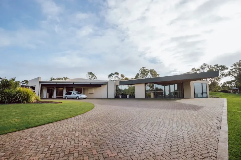 Wide view of the paved brick driveway and porte-cochère entrance with a silver hearse parked outside Geelong Memorial Park Chapel in Mount Duneed.