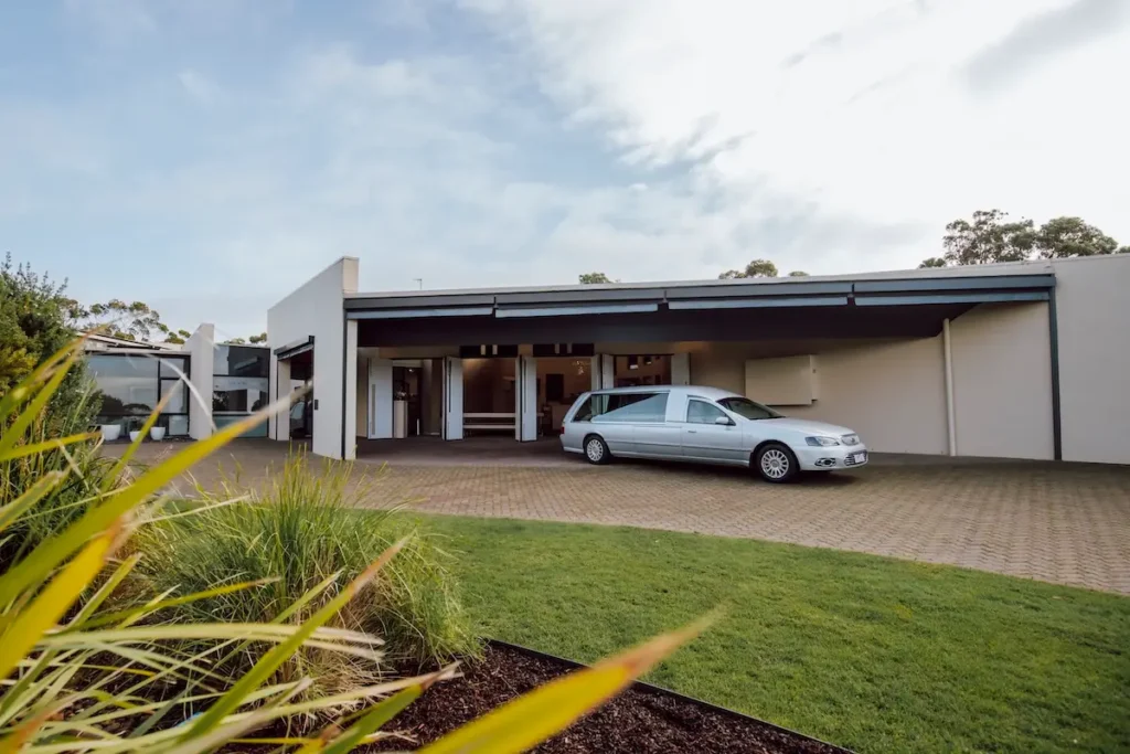 Silver funeral hearse parked under the covered entrance canopy outside Geelong Memorial Park Chapel, coordinated by Jonathan Hepner Funerals.