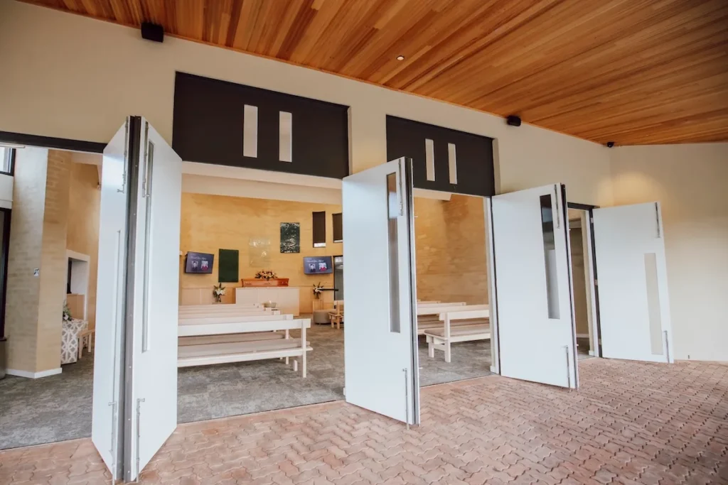 Large white bi-fold doors open under a timber-lined ceiling, looking directly into the bright chapel sanctuary at 42/110 Burvilles Rd, Mount Duneed.