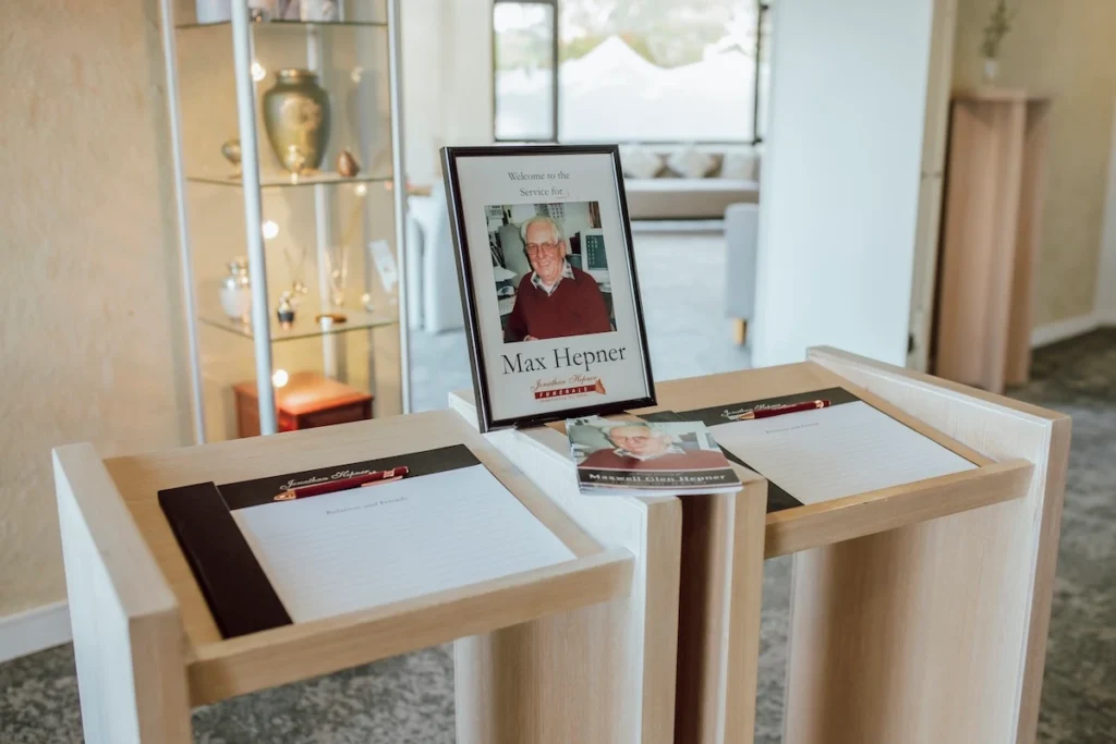 Light timber welcome desk with condolence registers and a framed tribute display in the foyer at Geelong Memorial Park Chapel.