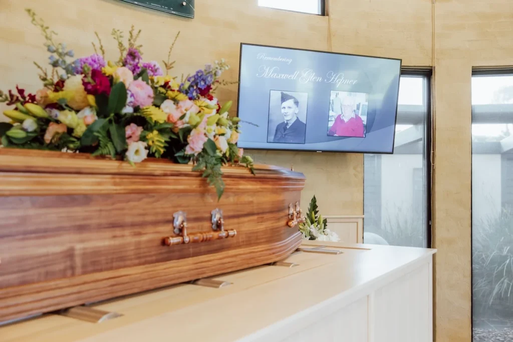 Close view of a polished wooden casket adorned with colourful flowers on the catafalque inside Geelong Memorial Park Chapel, available through Jonathan Hepner Funerals.