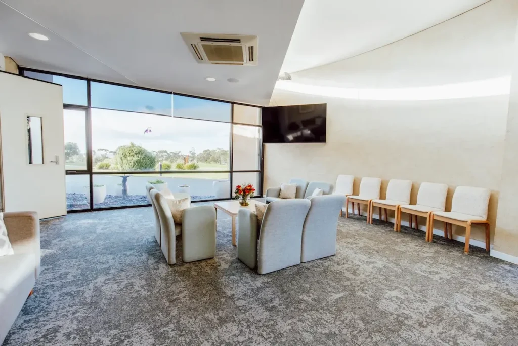 Bright family lounge with large window views across memorial gardens and overhead TV screen, available through Jonathan Hepner Funerals.