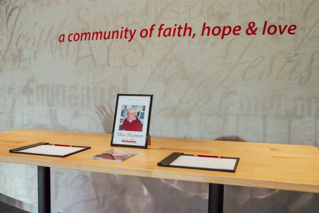 Light timber welcome desk in the foyer set up with condolence registers and a framed tribute display at Waurn Ponds Community Chapel, 48 Waurnvale Dr, Belmont.